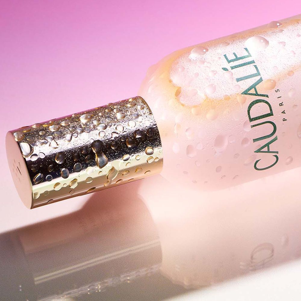 Primo piano di una bottiglia Caudalie Beauty Elixir sdraiata con gocce d'acqua.