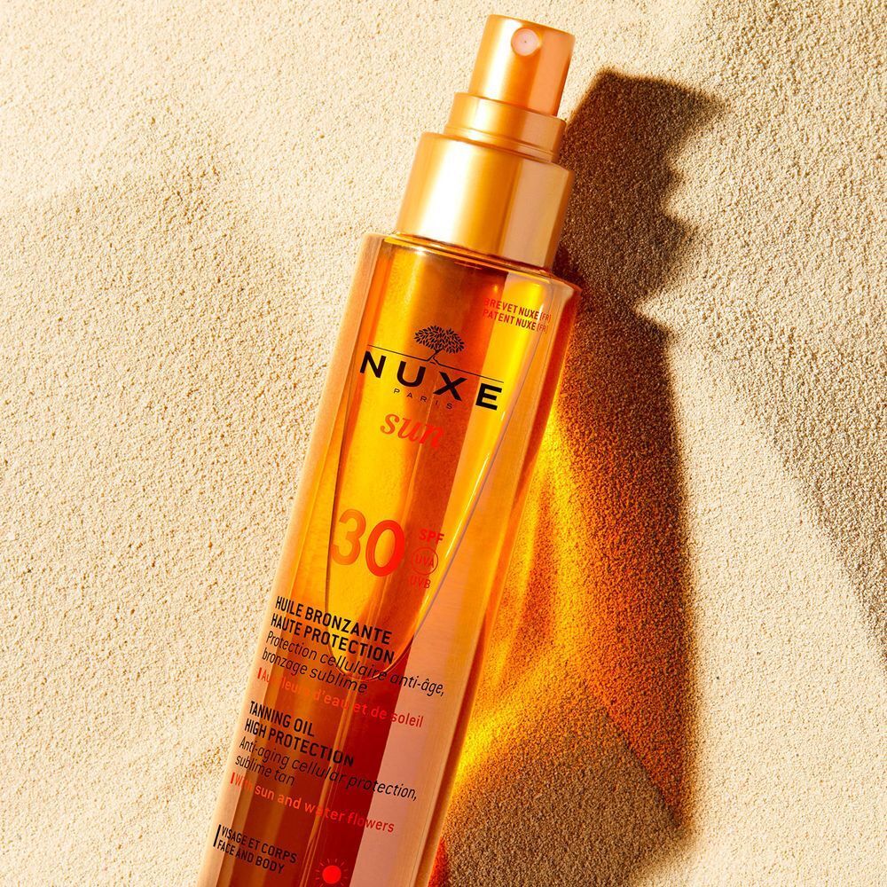 Olio Nuxe Sun SPF 30 in un flacone spray sulla sabbia.