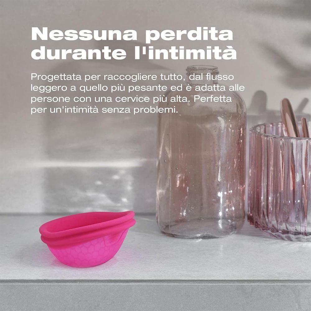 Coppetta mestruale rosa su uno scaffale accanto a contenitori di vetro.