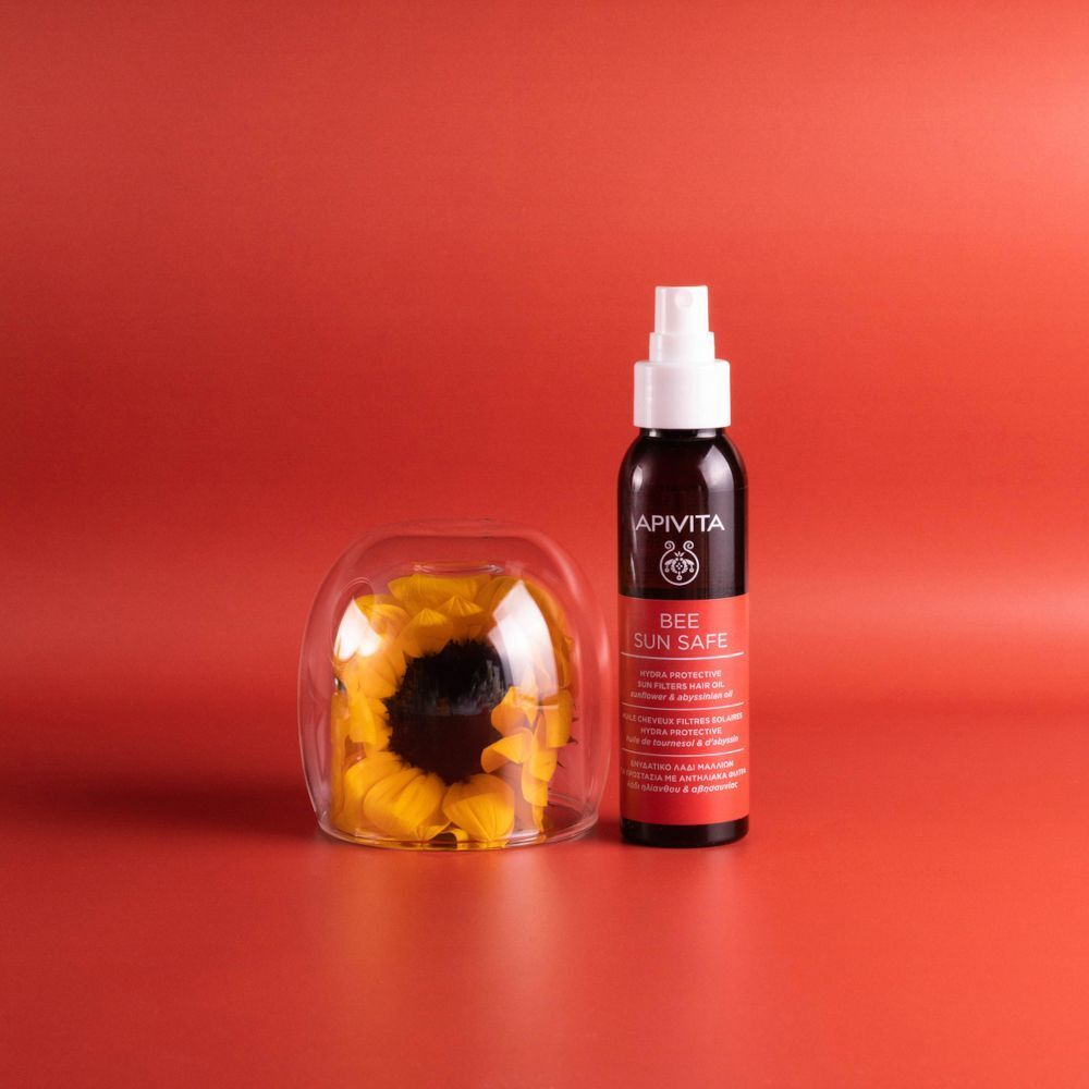 Olio capelli protettivo solare APIVITA accanto a un vaso di vetro con un girasole.