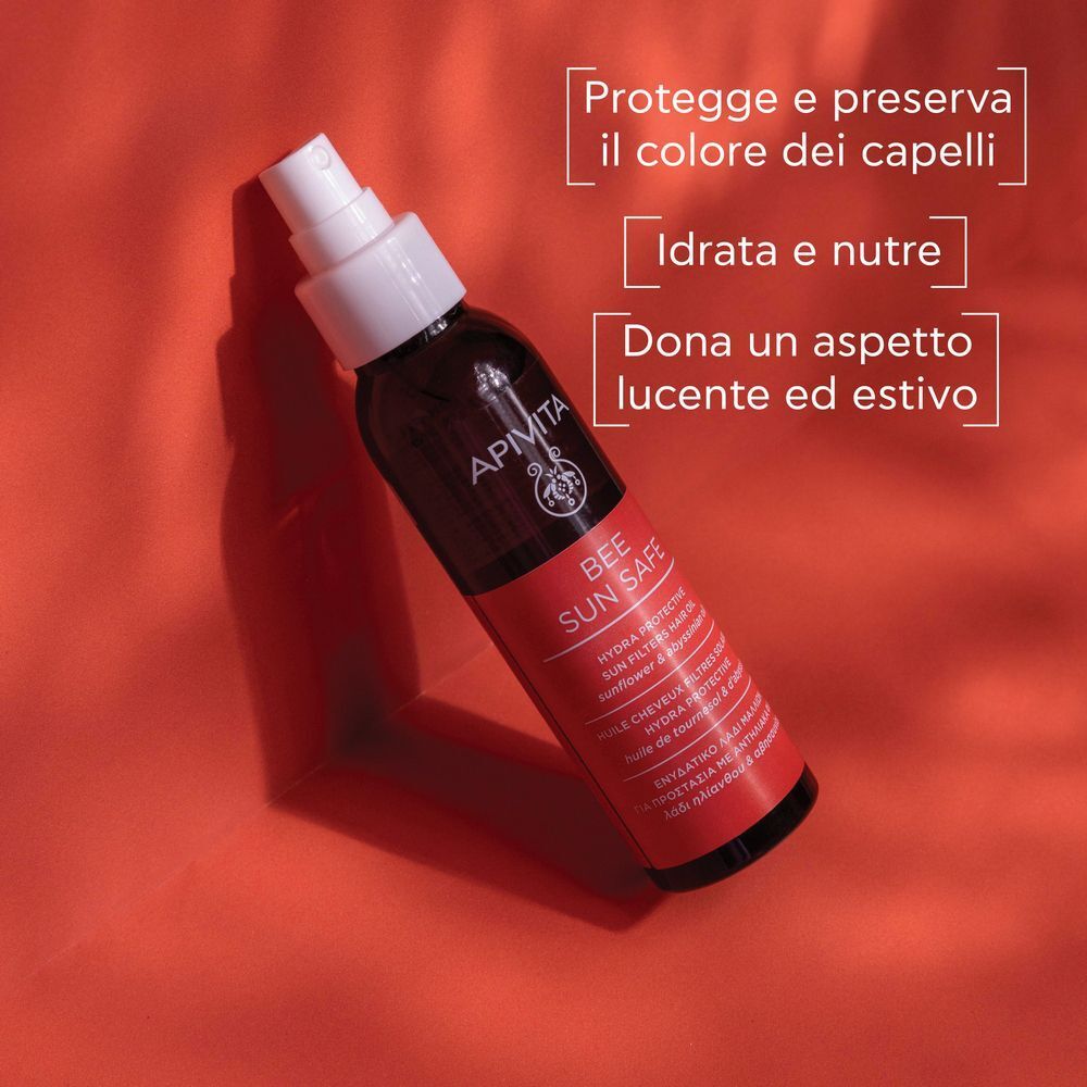 Flacone di olio capelli solare APIVITA con spray, su sfondo rosso.