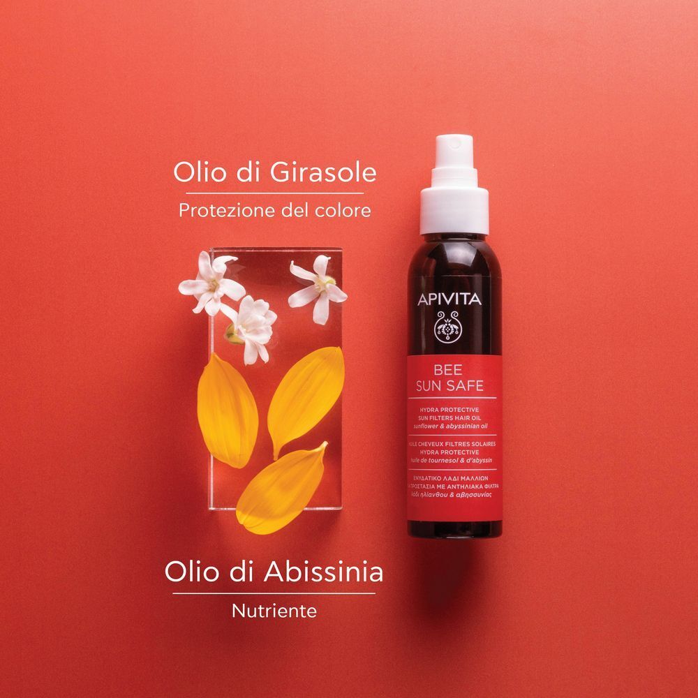 Flacone di olio capelli solare APIVITA accanto a petali e fiori di girasole.