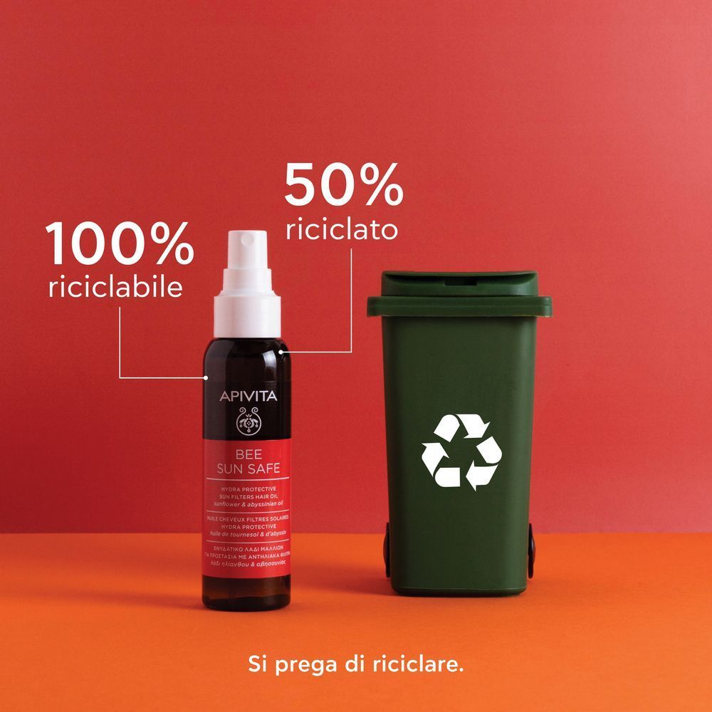 Flacone di olio capelli solare APIVITA accanto a un bidone della spazzatura verde con simbolo di riciclo.