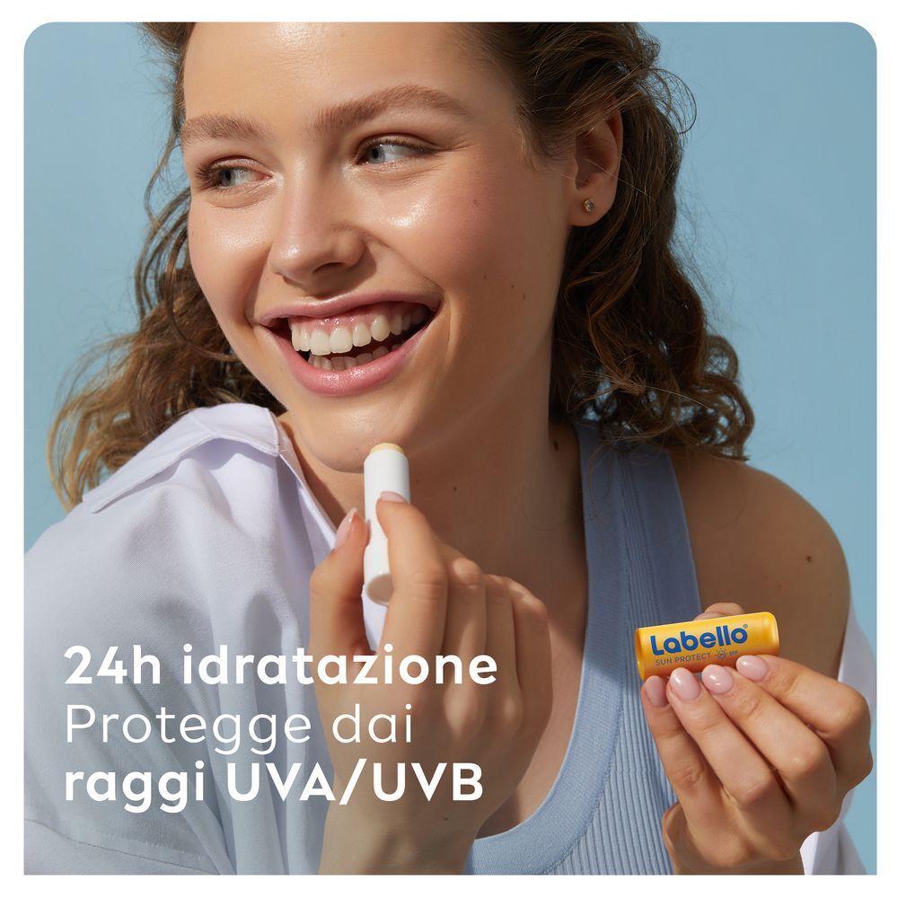 Donna applica balsamo labbra Labello Sun Protect SPF30. Offre 24h idratazione e protezione UVA/UVB.