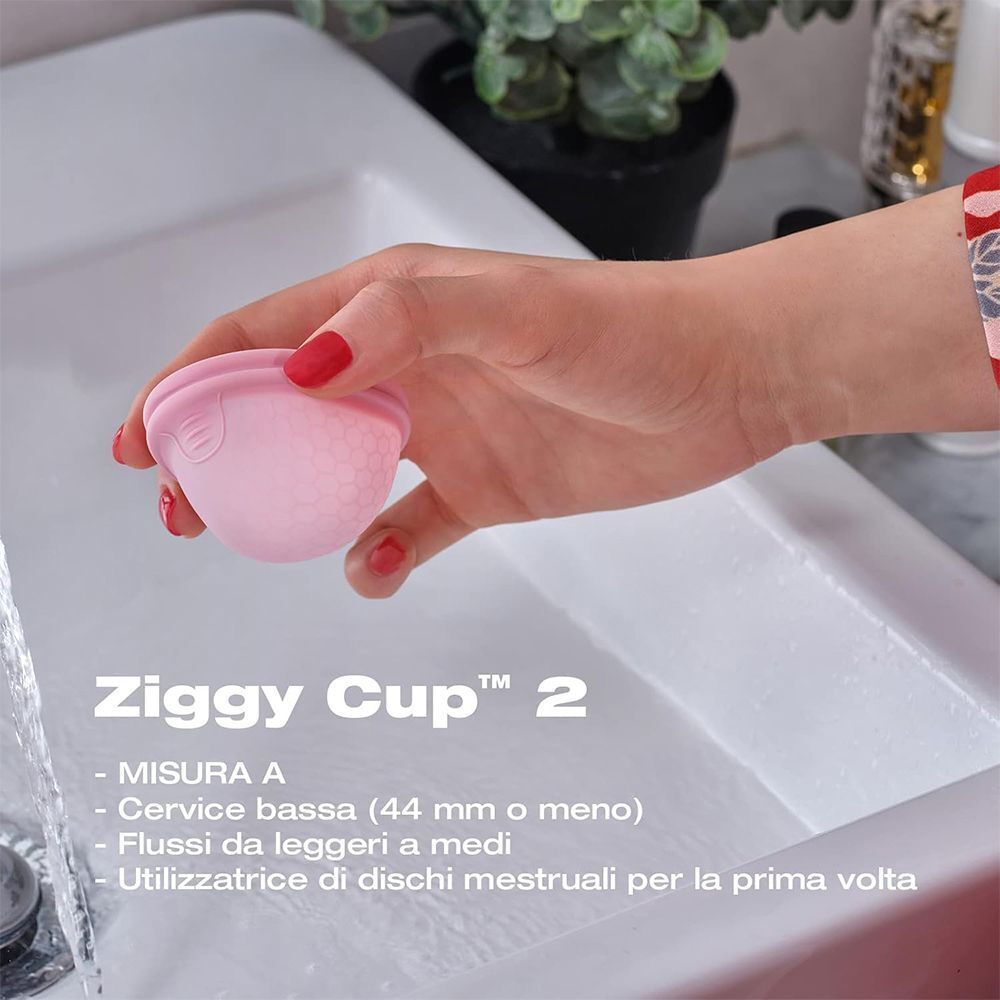 Mano che tiene una coppetta mestruale rosa sopra un lavandino.