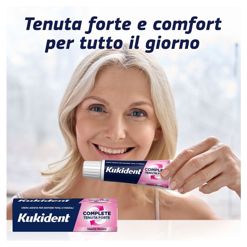 Donna sorridente tiene un tubetto di crema adesiva Kukident Complete. Altra confezione in basso.