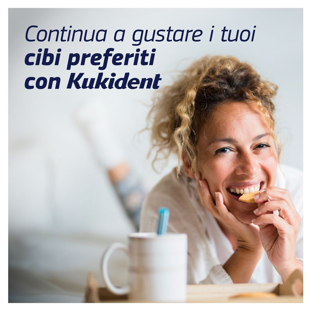 Donna mangia un biscotto con gusto, tazza e Kukident in primo piano.