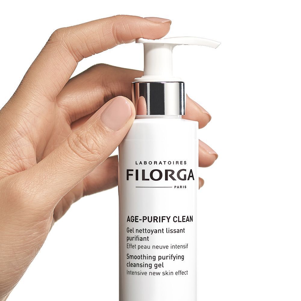 Una mano tiene un flacone a pompa bianco di gel detergente FILORGA Age-Purify Clean.