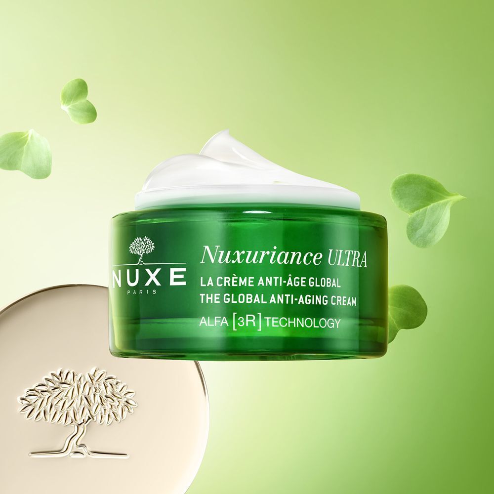 Barattolo di crema Nuxe Nuxuriance Ultra, coperchio dorato, circondato da foglie verdi.