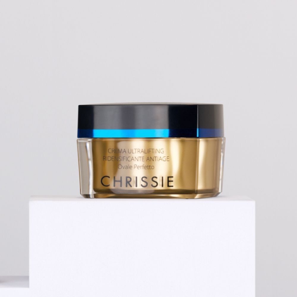 Vasetto dorato con tappo nero e fascia blu, posizionato su un cubo bianco.