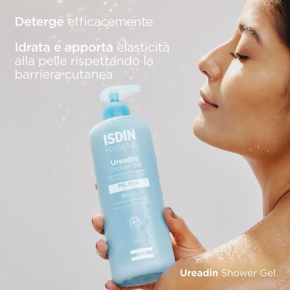 Una donna tiene il gel doccia ISDIN Ureadin sotto la doccia. Testo: 'Deterge efficacemente'.