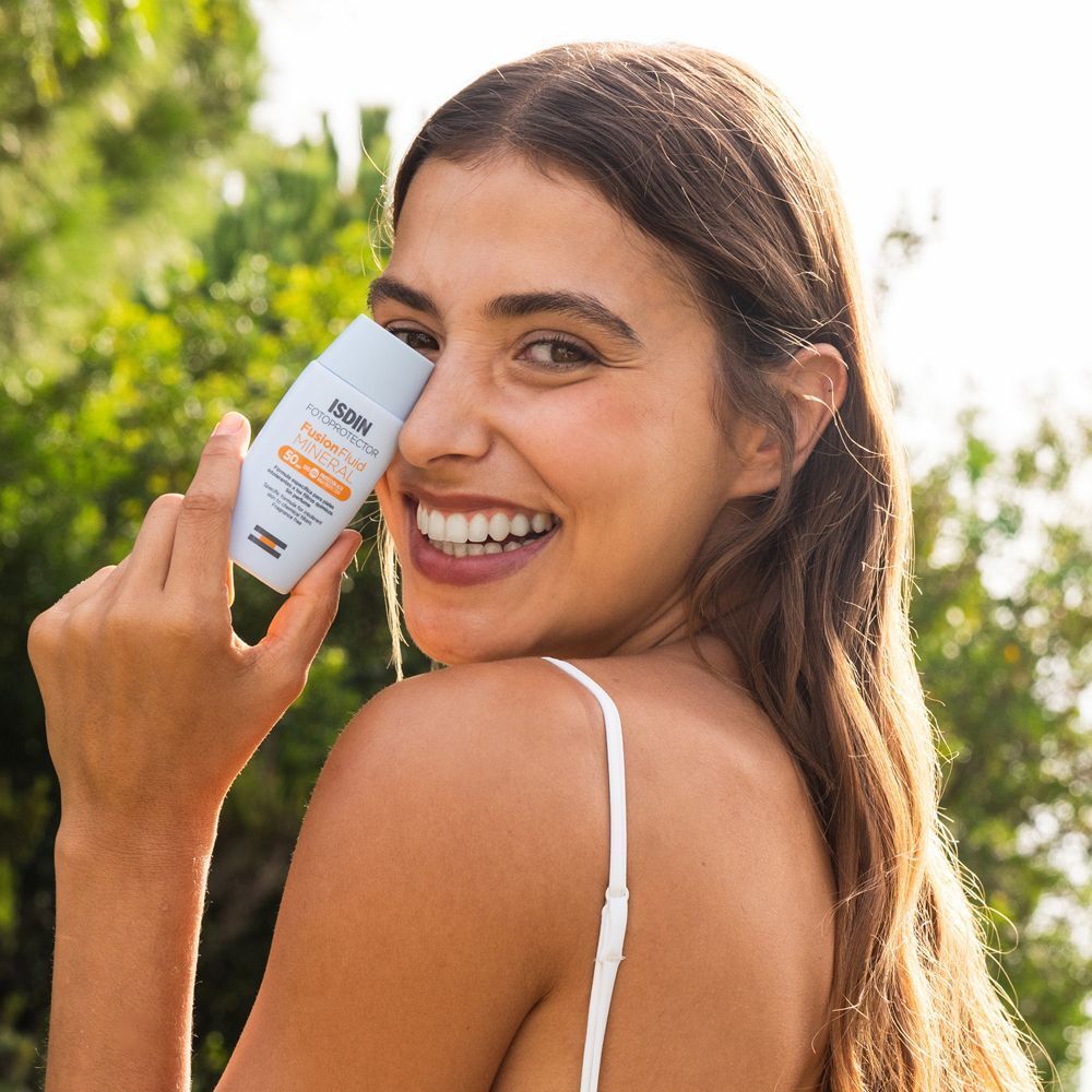 Una donna tiene in mano un flacone ISDIN Fotoprotector Fusion Fluid Mineral SPF50 davanti al viso.