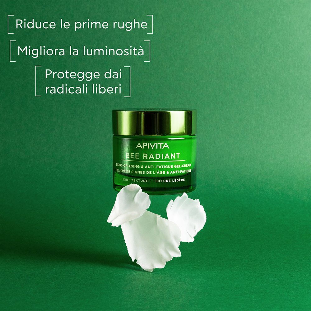 Vasetto verde di Gel-Crema APIVITA Bee Radiant accanto a petali di fiori bianchi.