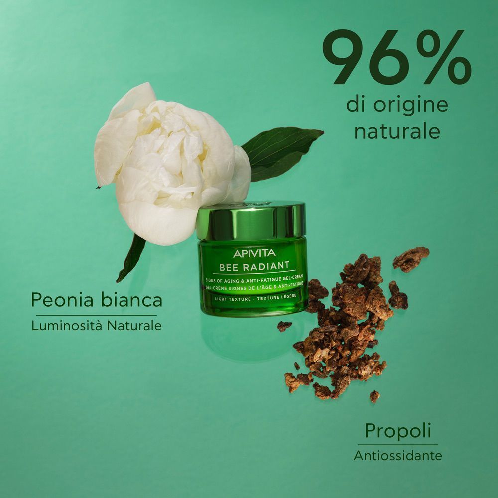 Vaso verde APIVITA BEE RADIANT crema viso, accanto a peonia bianca e propoli.