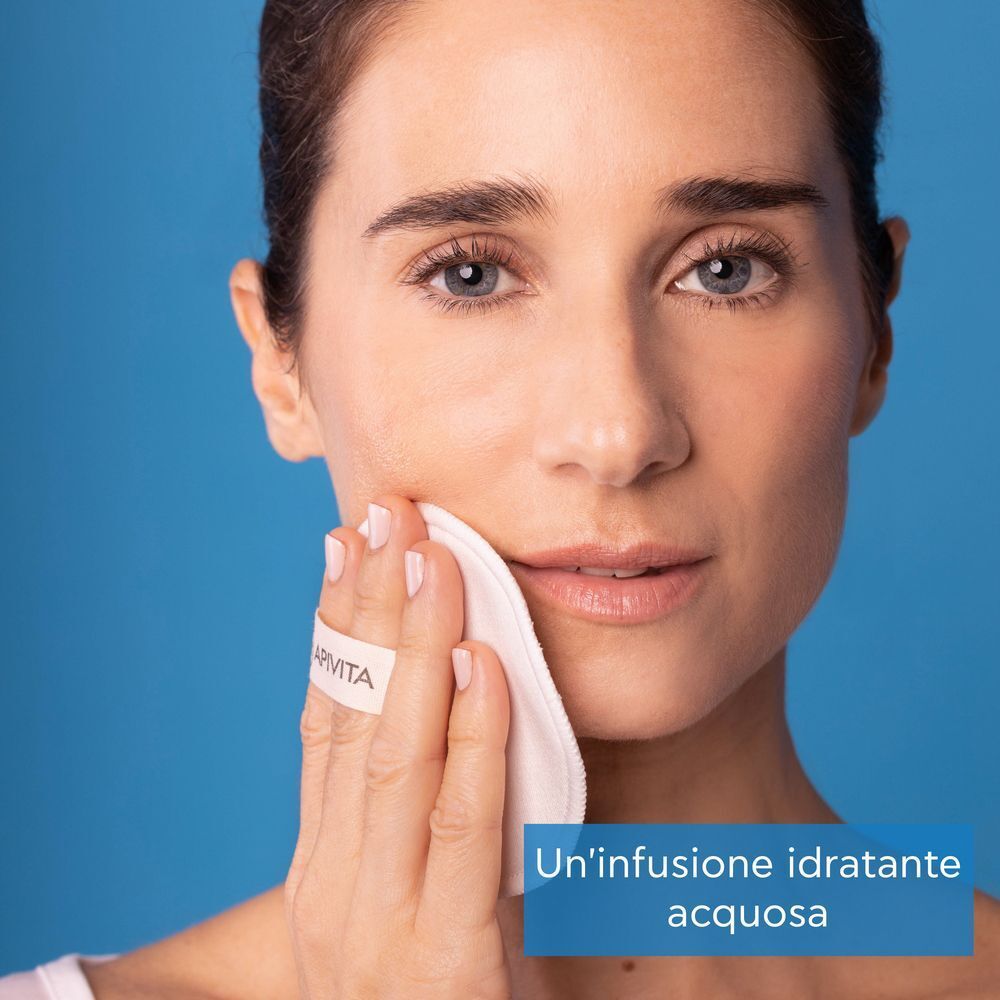 Una donna che si pulisce il viso con un dischetto di cotone APIVITA.