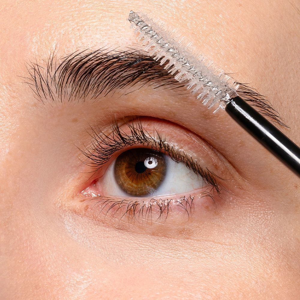 Primo piano di un occhio, un applicatore di mascara trasparente sulle sopracciglia.