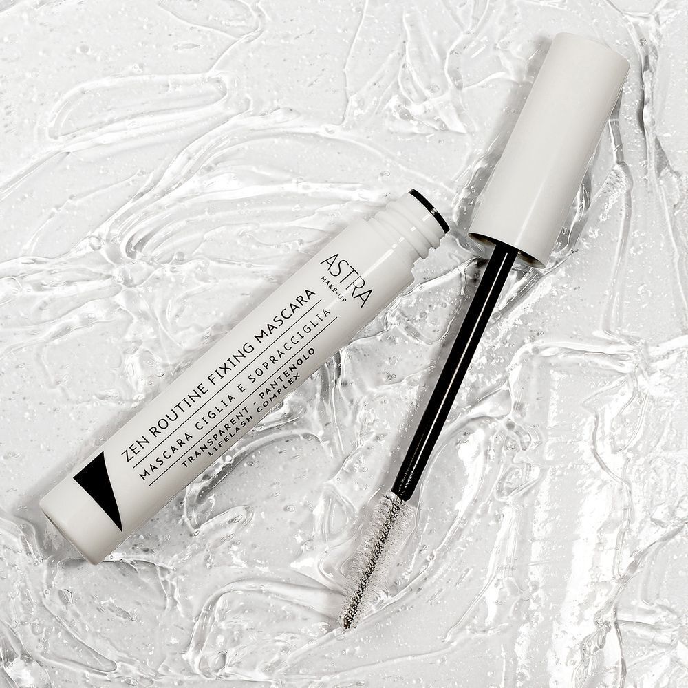 Un Mascara Fixateur ASTRA Make-Up Zen Routine trasparente aperto giace su una superficie testurizzata.