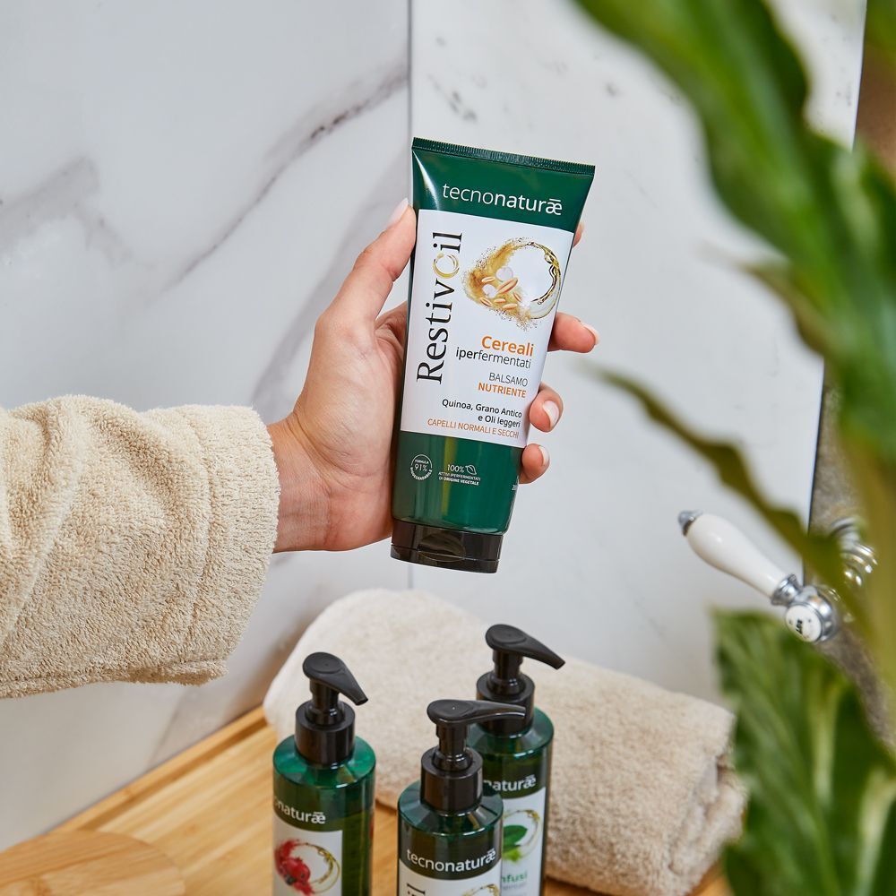 Mano che tiene un tubo Restivoil Tecnonaturae Balsamo Nutriente in un bagno.