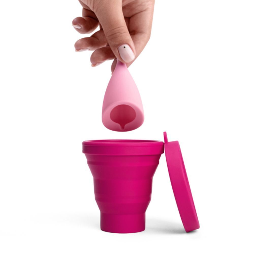 Mano che tiene una coppetta mestruale rosa sopra una coppetta sterilizzatrice pieghevole rosa.