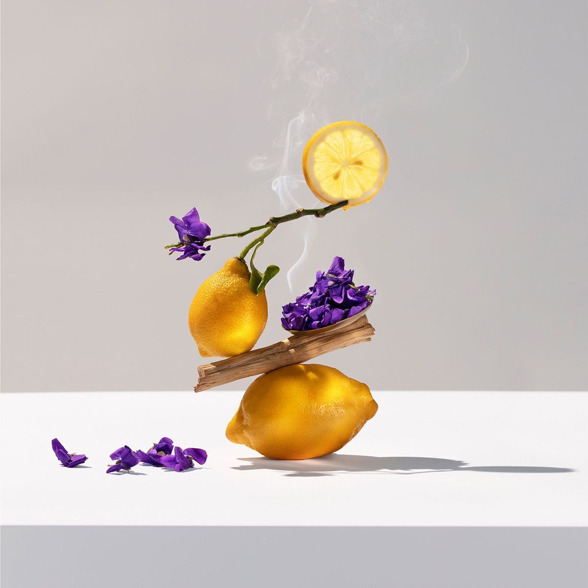Limoni, fiori viola e un pezzo di legno formano una piramide, con vapore che sale.
