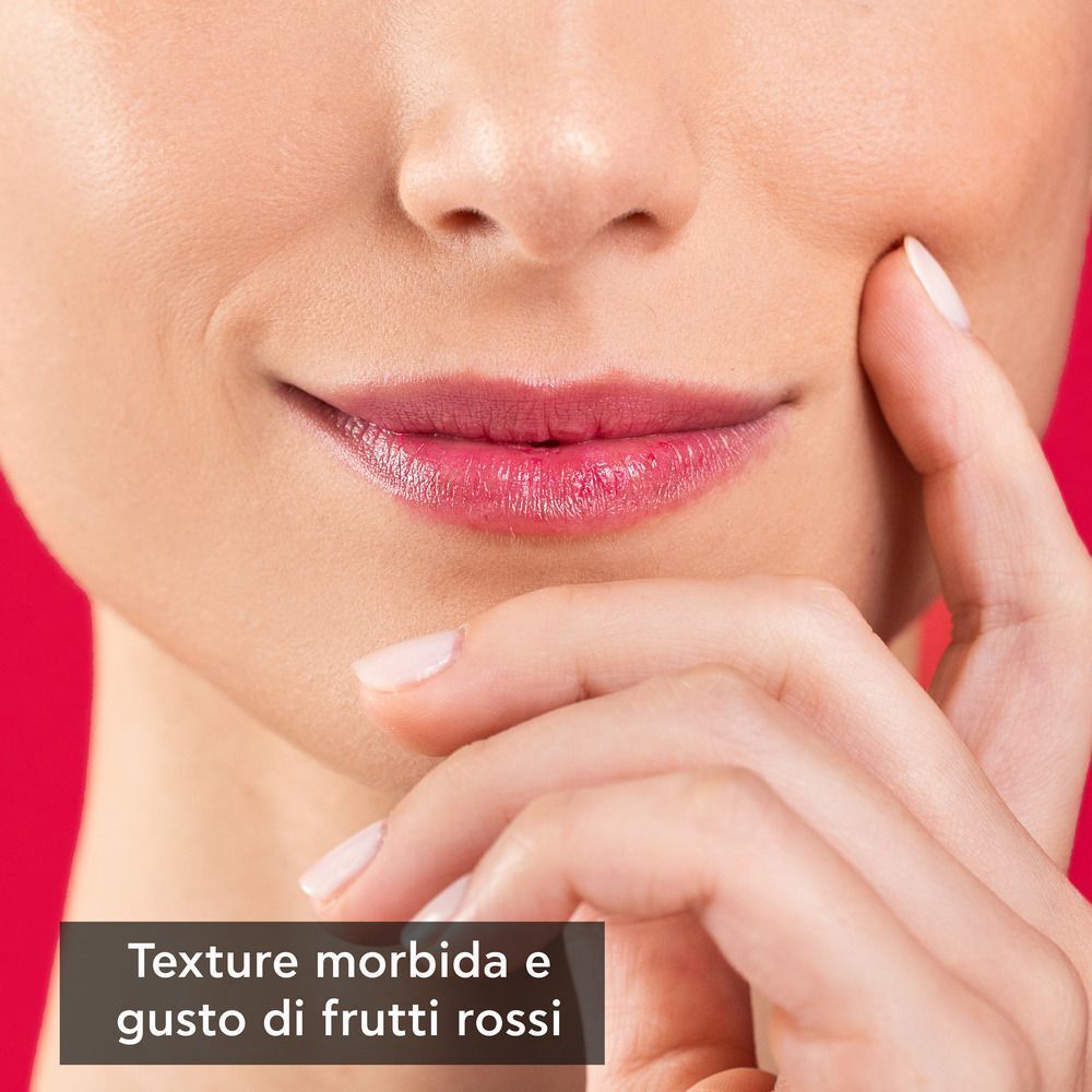 Primo piano di una donna che indossa un balsamo labbra rosso e al gusto di frutti rossi.