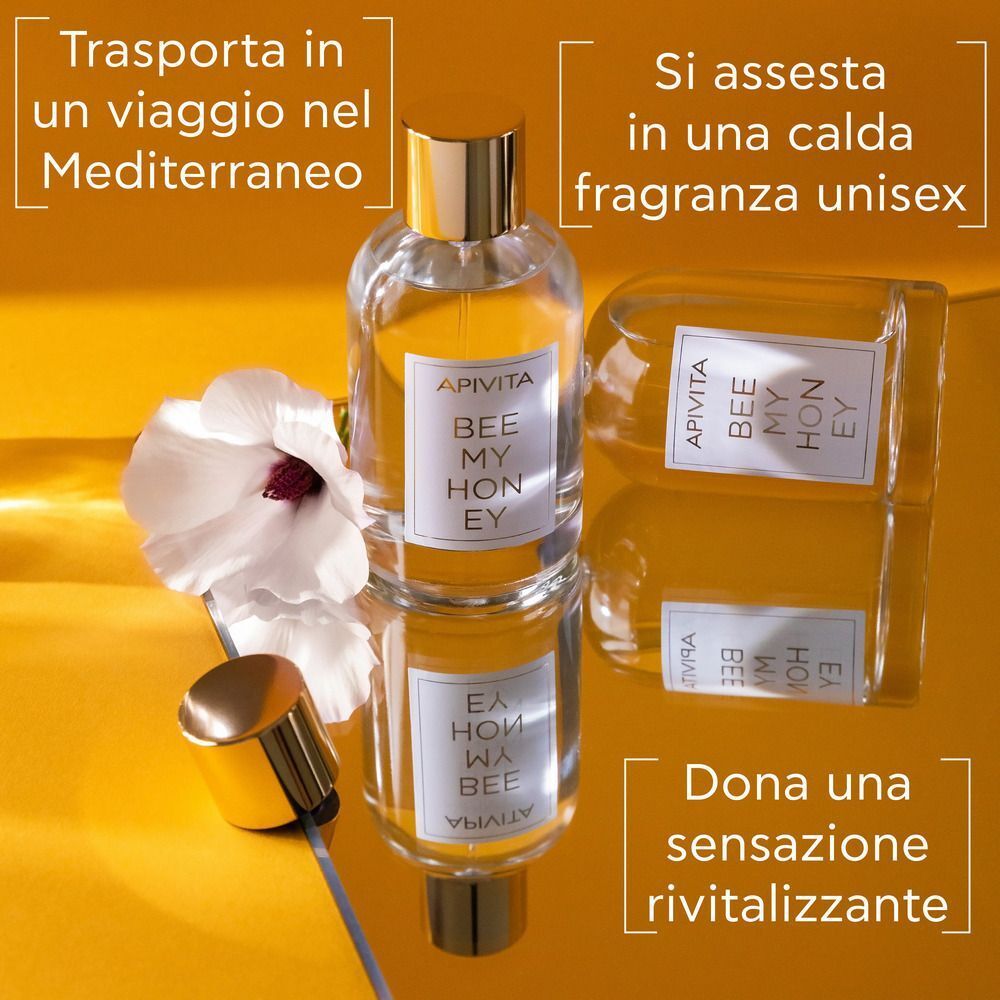 Flacone di APIVITA Bee My Honey Eau de Toilette accanto a un flacone capovolto e un fiore bianco.