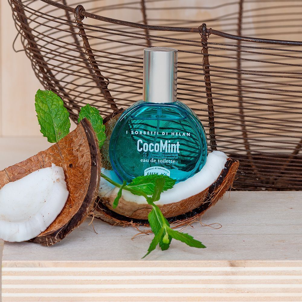 Un flacone in vetro blu con tappo argentato, posizionato in metà di cocco con foglie di menta.