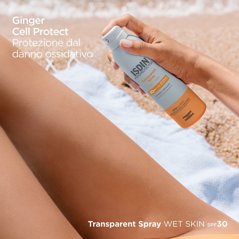 Flacone spray ISDIN Fotoprotector Transparent Spray Wet Skin SPF 30 sulla spiaggia.