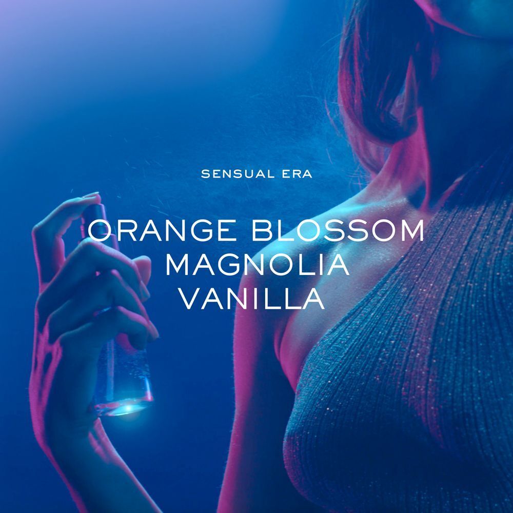 Primo piano di una donna che spruzza il profumo Nuxe Sensual Era. Note: Fiore d'arancio, Magnolia, Vaniglia.