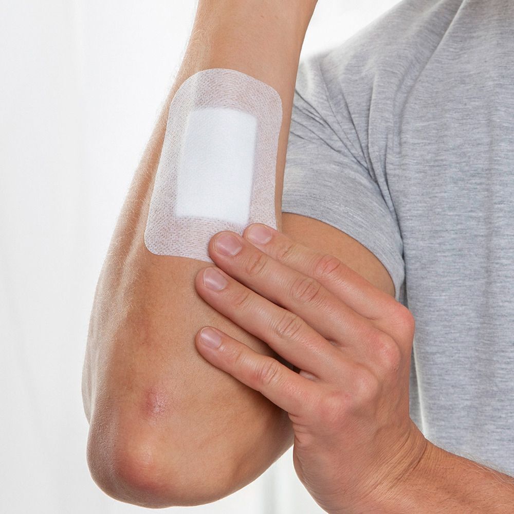 Una persona applica una medicazione post-operatoria sterile e assorbente sul gomito.