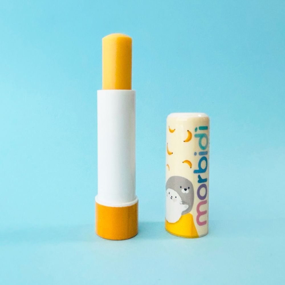 Un stick di balsamo labbra Morbidi, esteso, accanto al suo cappuccio con banane e una foca.