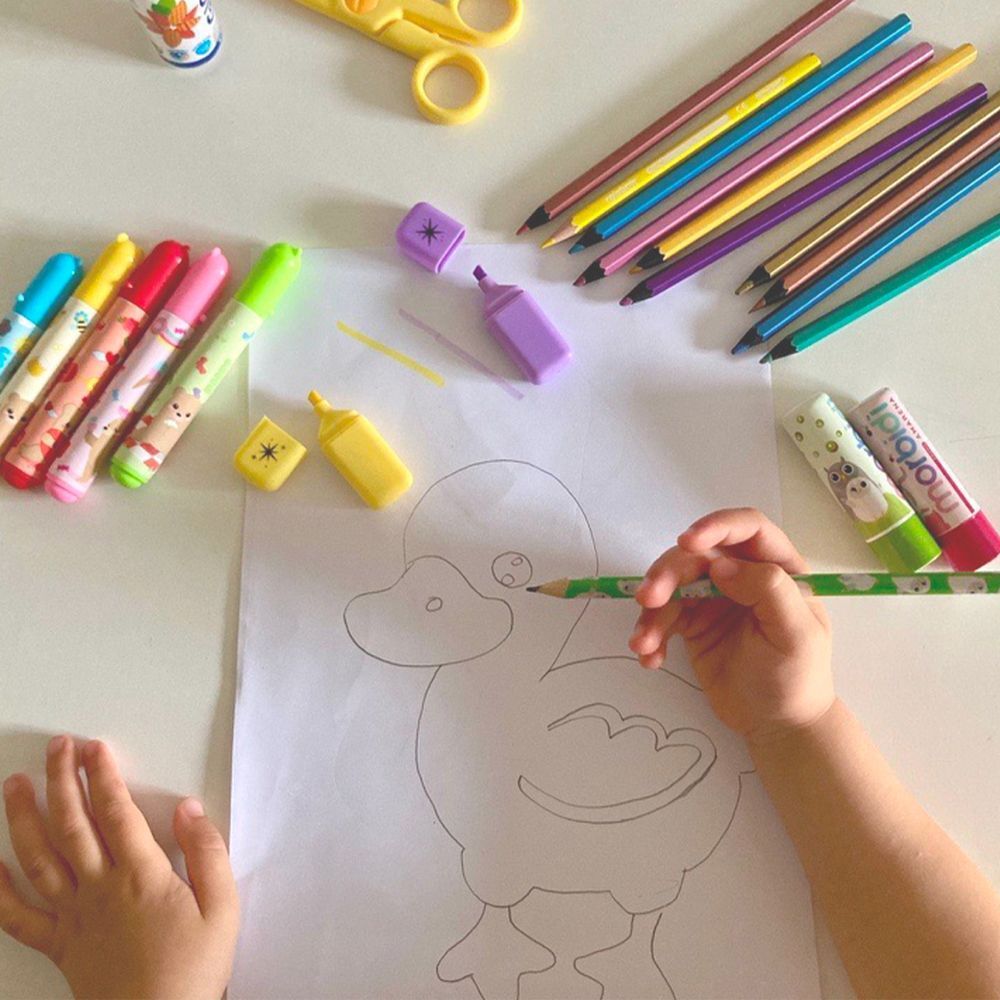 Un bambino disegna un'anatra, circondato da matite, pennarelli e due balsami labbra.