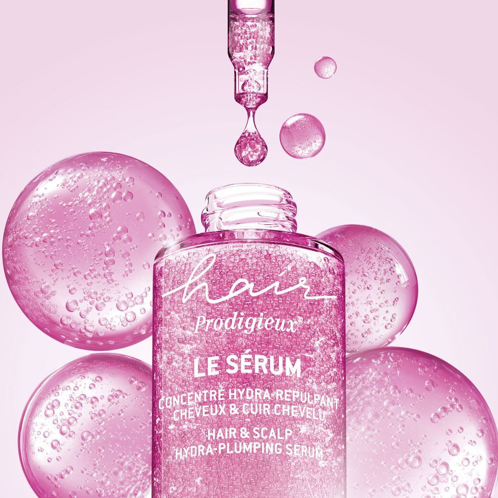Flacone di siero per capelli Nuxe Hair Prodigieux con contagocce, circondato da bolle rosa.