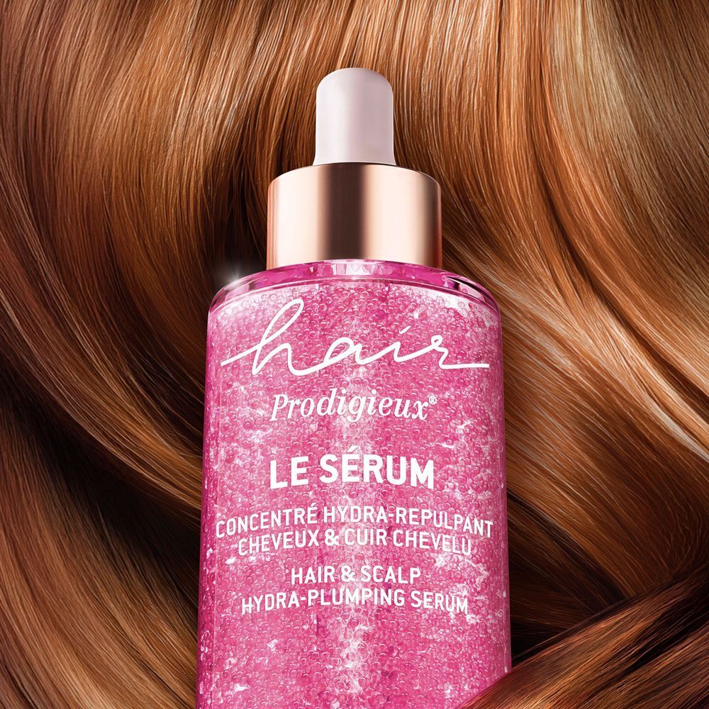 Flacone di Nuxe Hair Prodigieux Siero Capelli Idratante Volumizzante davanti a capelli castani lucidi.
