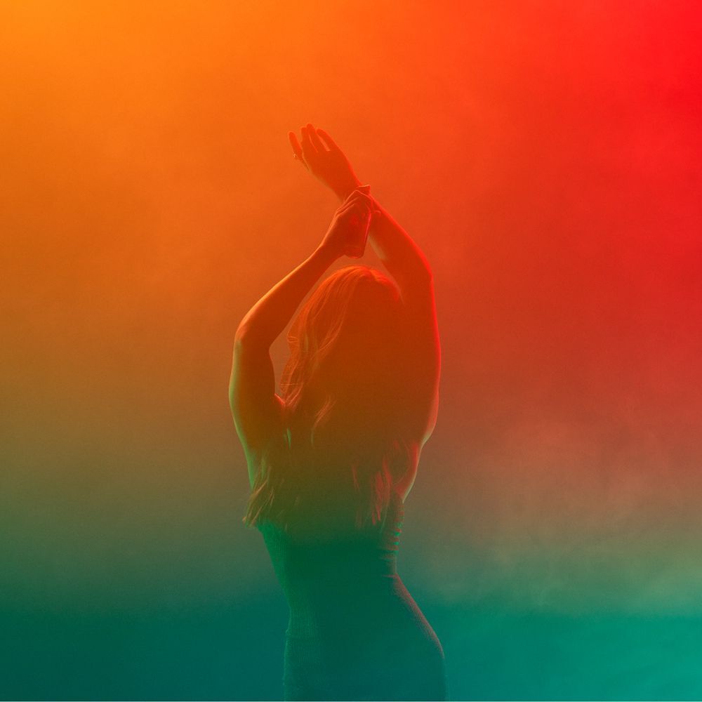 Silhouette di una donna con le braccia alzate in una nebbia colorata.