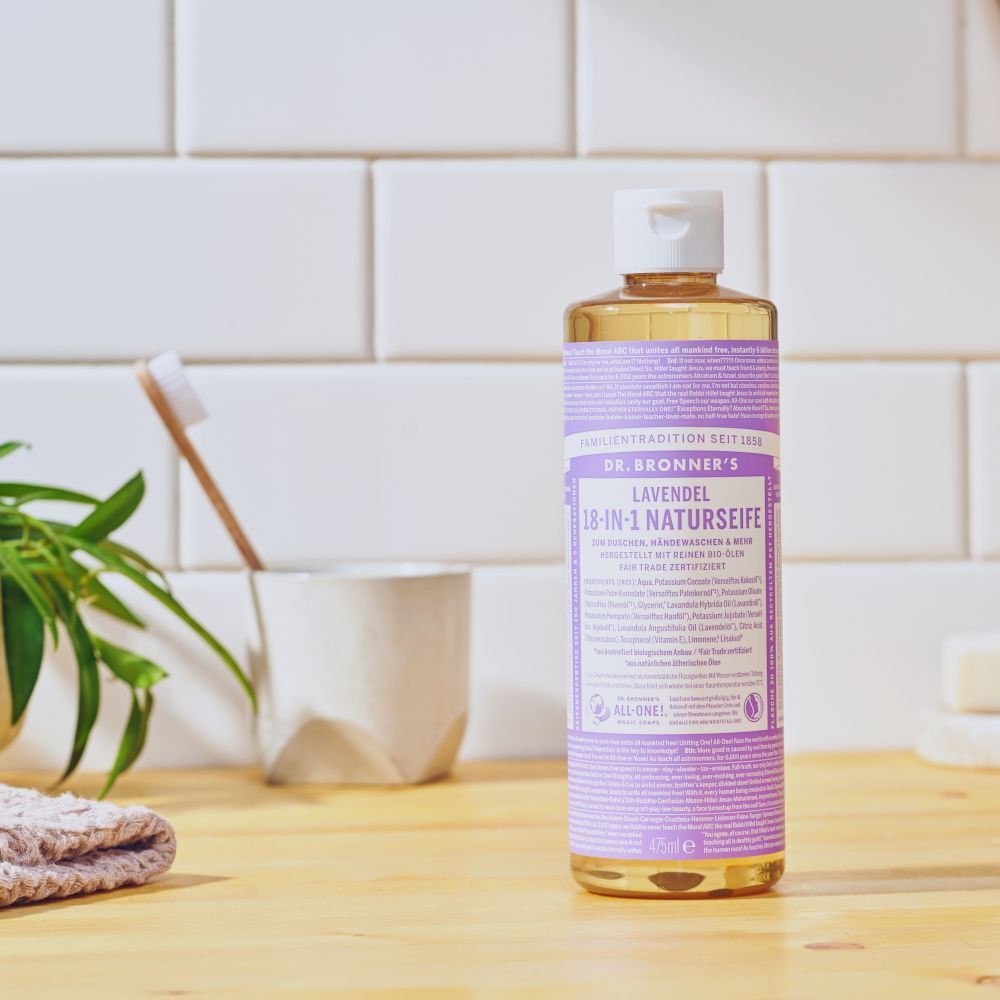 Sapone Liquido Bio 18-in-1 Lavanda Dr. Bronner's su un mobiletto del bagno vicino a uno spazzolino.
