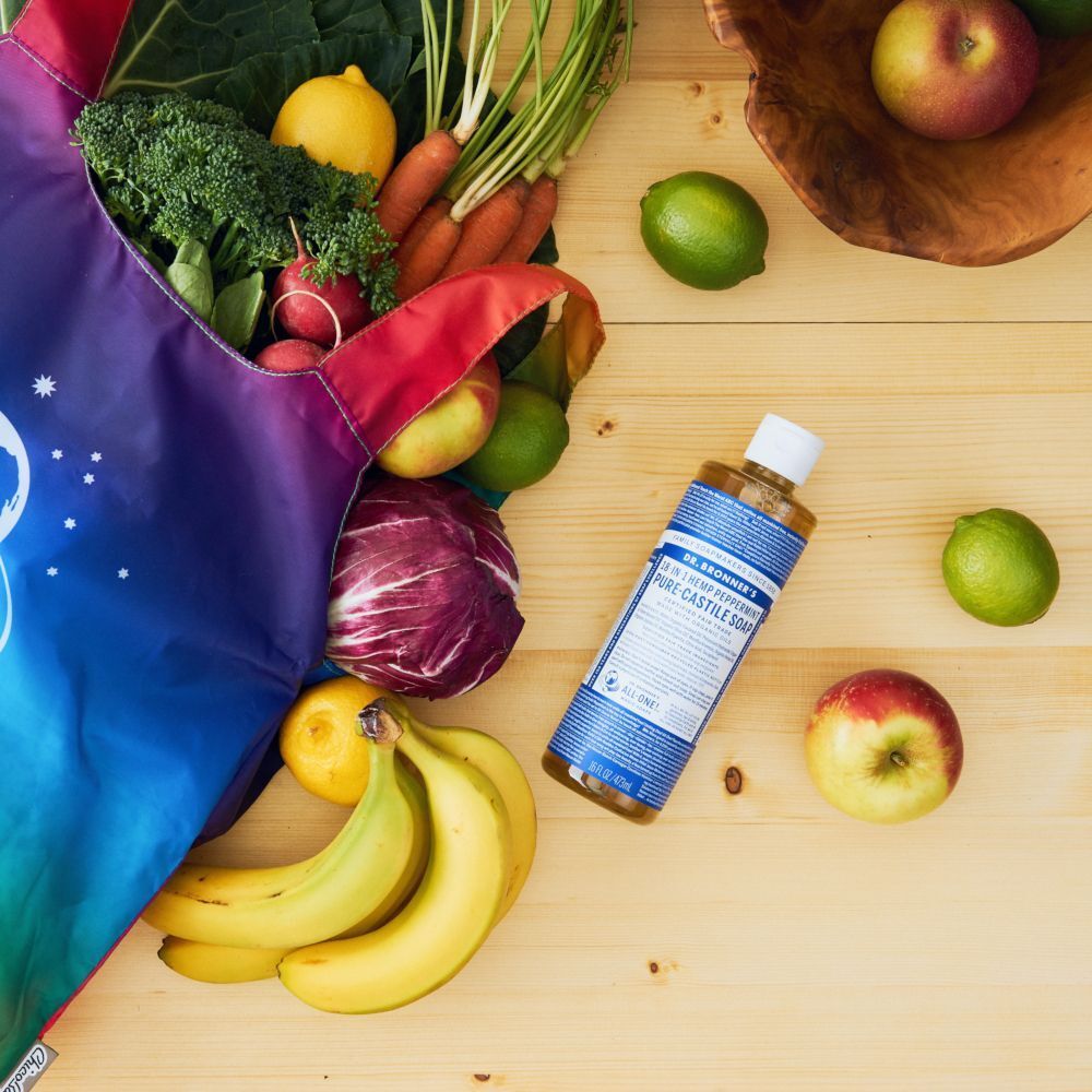 Flacone di sapone Dr. Bronner's menta piperita vicino a una borsa della spesa con frutta e verdura.