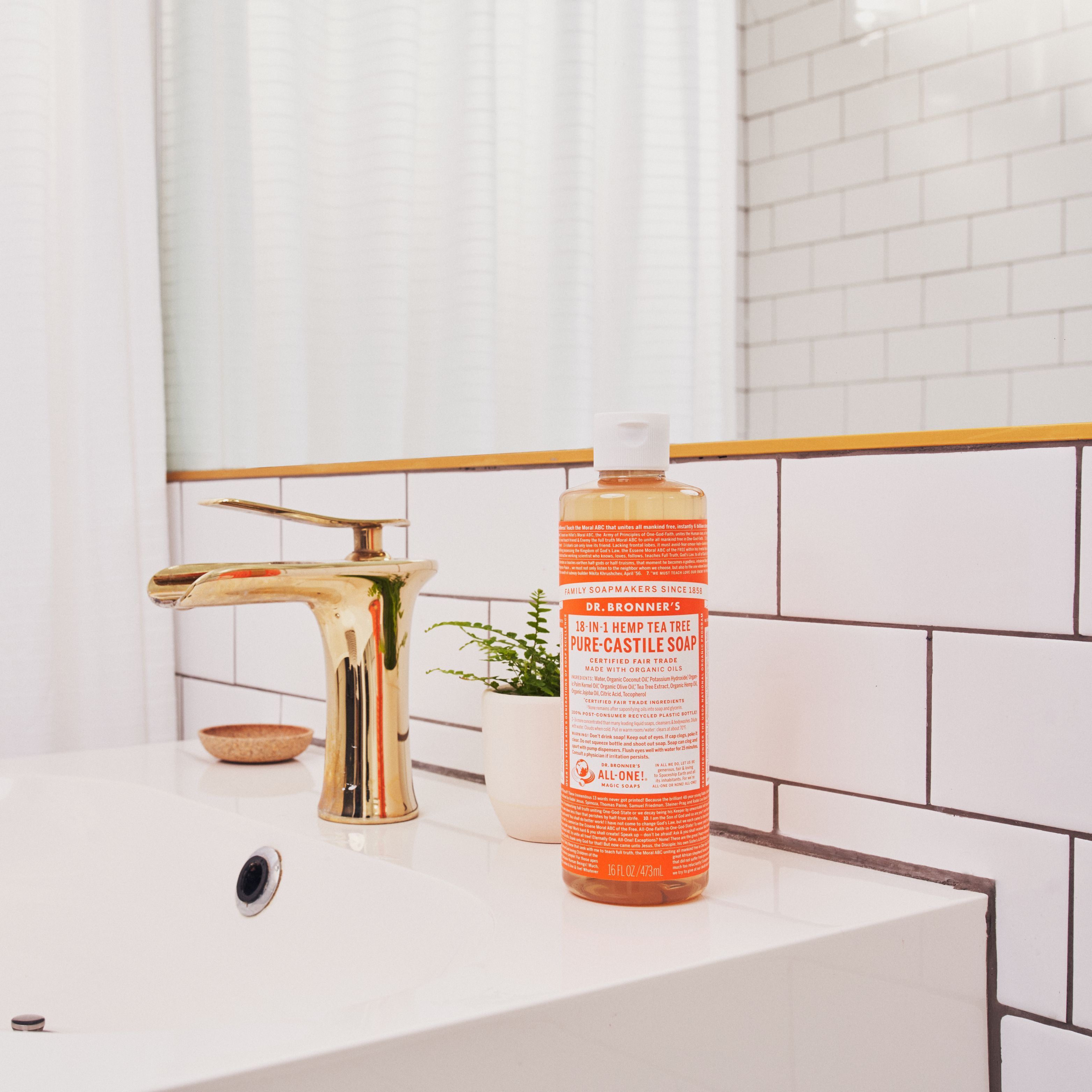 Sapone liquido biologico Dr. Bronner's 18-in-1 Tea Tree vicino a un rubinetto in un bagno.