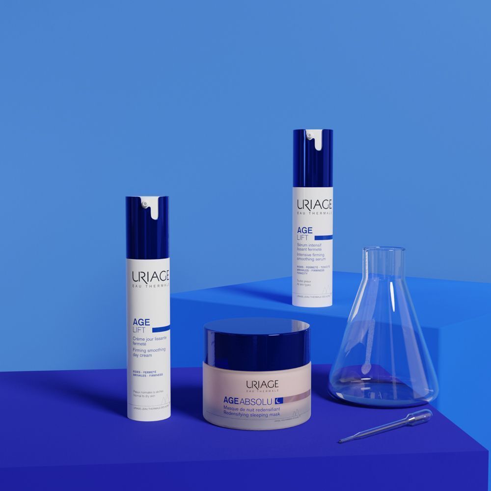 Tre contenitori cosmetici Uriage Age Lift: due dispenser a pompa e un vasetto. Accanto, un becher e una pipetta.