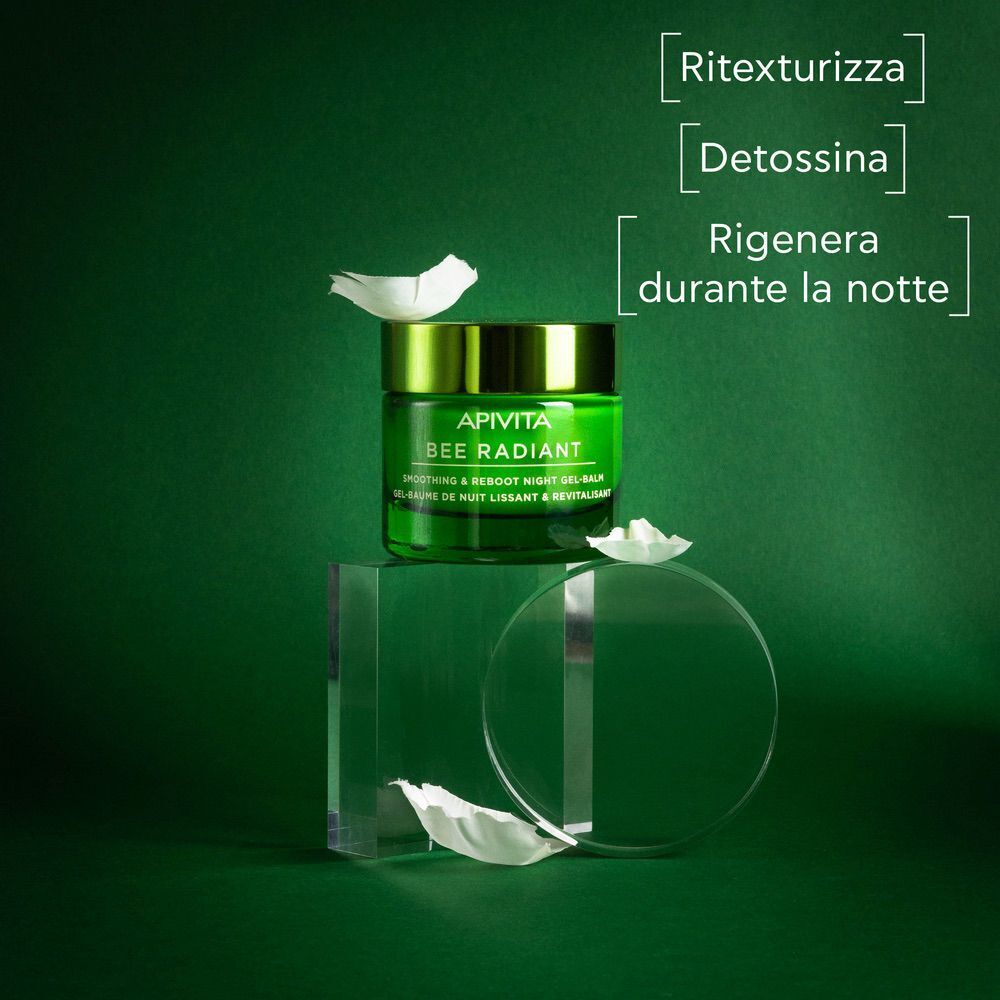 Vasetto verde Apivita Bee Radiant balsamo-gel notte su piedistallo in vetro, con petali.