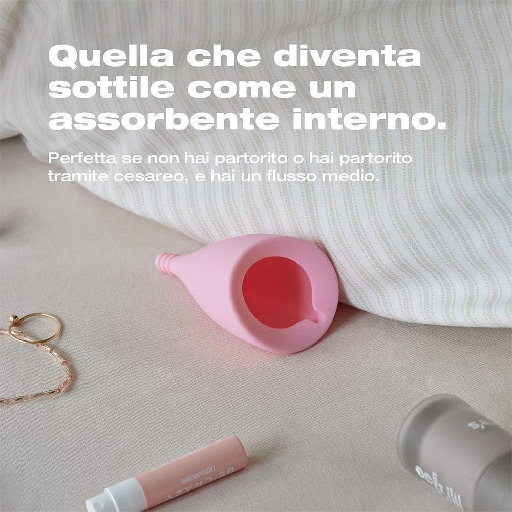 Coppetta mestruale rosa su una superficie di tessuto.