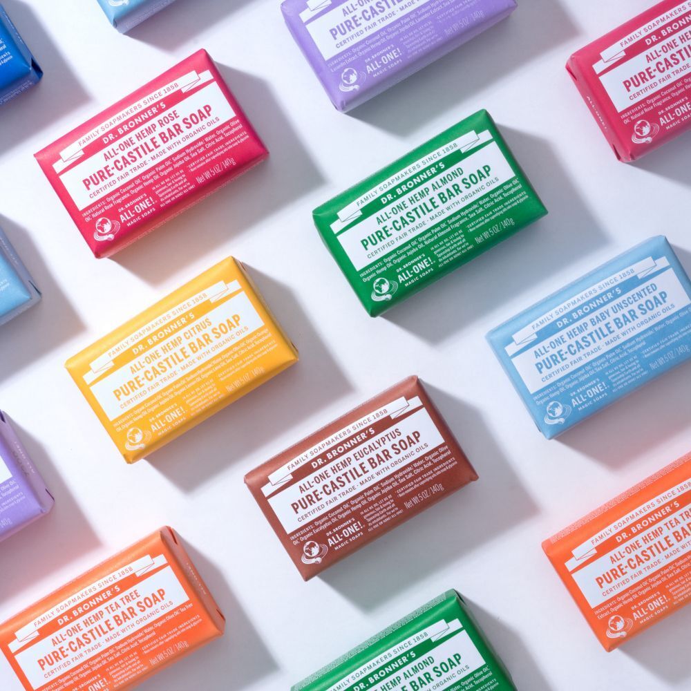 Varie saponette Dr. Bronner's in diversi colori e profumi, disposte in piano.