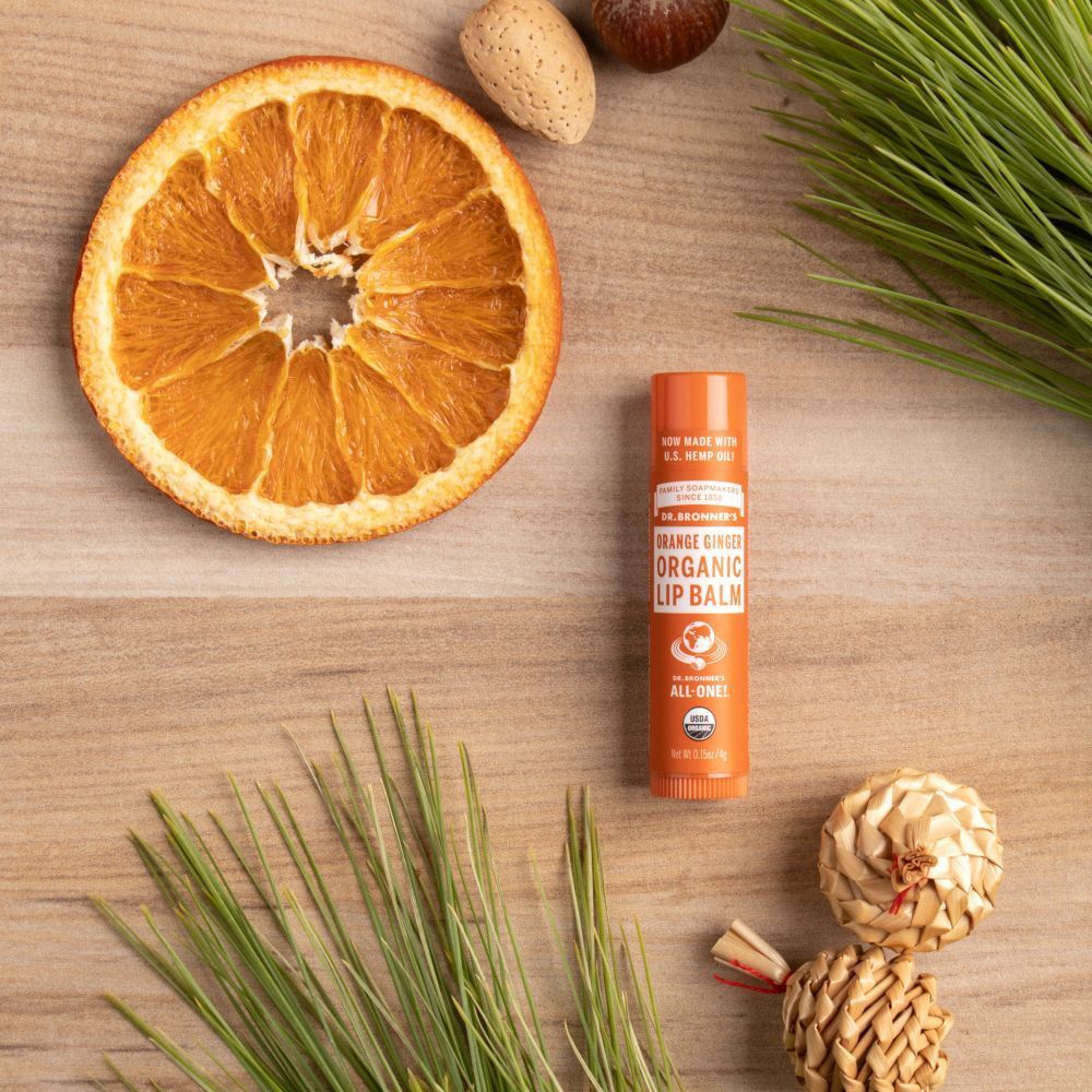 Un balsamo labbra bio Dr. Bronner's arancione vicino a una fetta d'arancia essiccata.