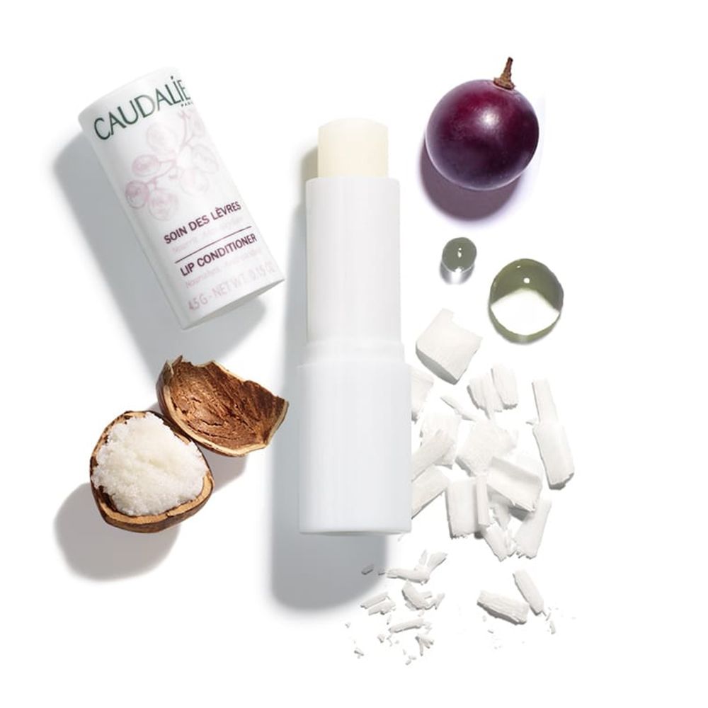 Stick per labbra, uva, gocce e pezzi di burro di karité. Sulla confezione è presente il marchio "CAUDALIE" e "SOIN DES LEVRES LIP CONDITIONER".