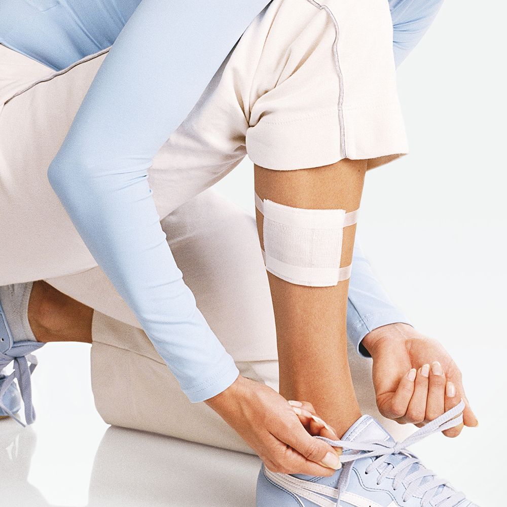 Persona con compressa sulla gamba. Compressa fissata con una fascia. La persona allaccia le scarpe.