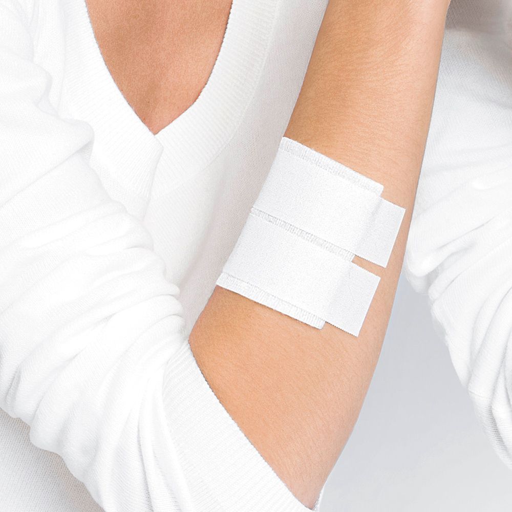 Braccio con due cerotti bianchi. Persona con maglia bianca. Cerotti applicati sul gomito.