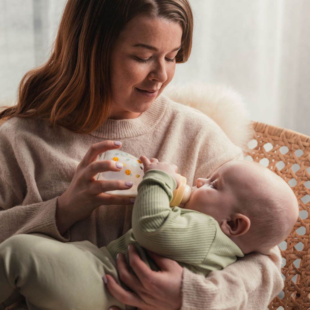 Una donna sta dando da mangiare a un bambino con un biberon. Il biberon ha un motivo a piccoli fiori gialli.