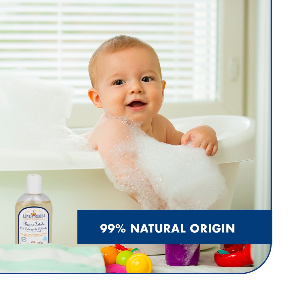 Bambino in vasca con schiuma. Flacone con etichetta sullo sfondo. Testo: 99% origine naturale.