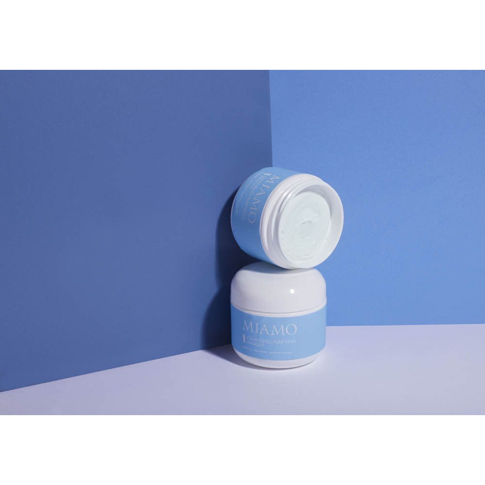 Due vasetti bianchi con etichetta blu. Scritta: MIAMO, CLEANSING-PURIFYING MASQUE. Un vasetto è aperto.