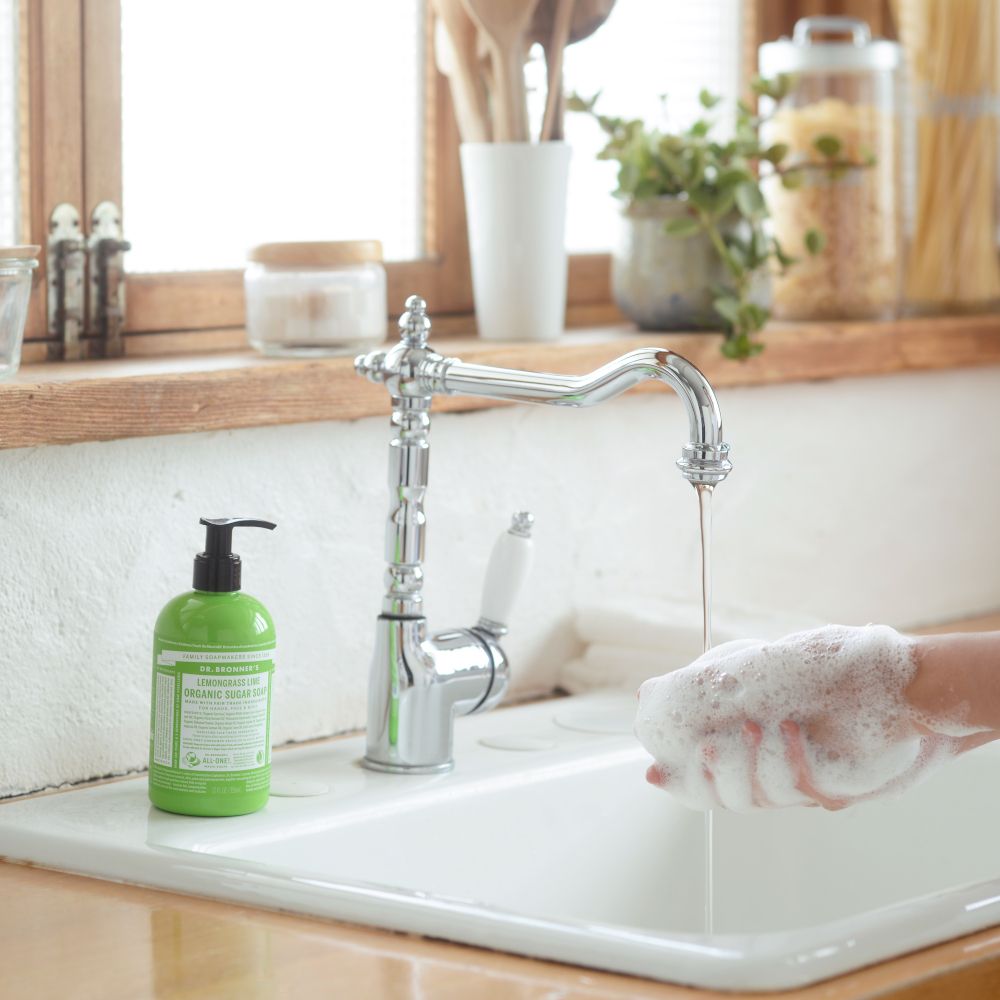 Flacone verde vicino al lavandino. Persona che si lava le mani. Rubinetto cromato.